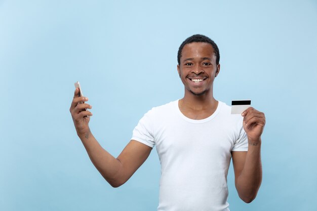 portrait of young african-american man in white shirt holding a card and smartphone.