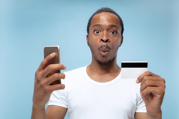 portrait of young african-american man in white shirt holding a card and smartphone.