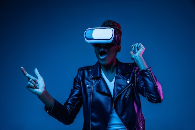 Портрет молодой афро-американской женщины, играющей в VR-очках в неоновом свете на синем.