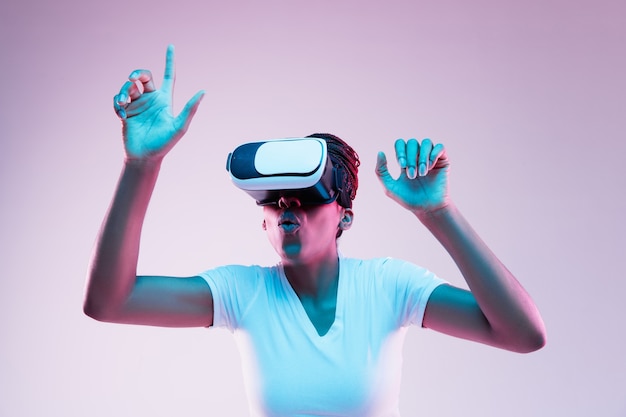 Free photo portrait of young african-american woman's playing in vr-glasses in neon light on gradient