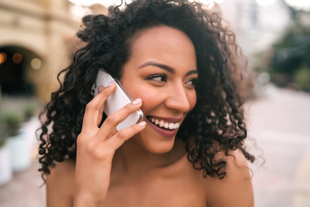 通りの屋外で電話で話している若いアフリカ系アメリカ人ラテン女性の肖像画。技術コンセプト。
