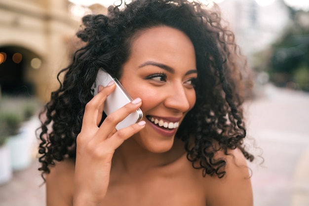 Portrait of young afro american latin woman talking on the phone outdoors in the street. Technology concept.