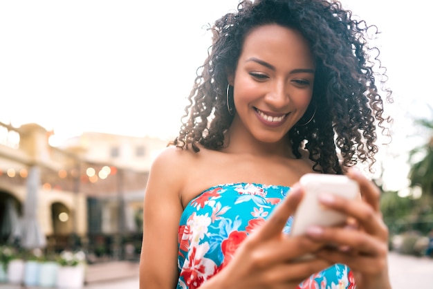 Портрет молодой афро-американской латинской женщины, использующей свой мобильный телефон на открытом воздухе на улице. Концепция технологии.