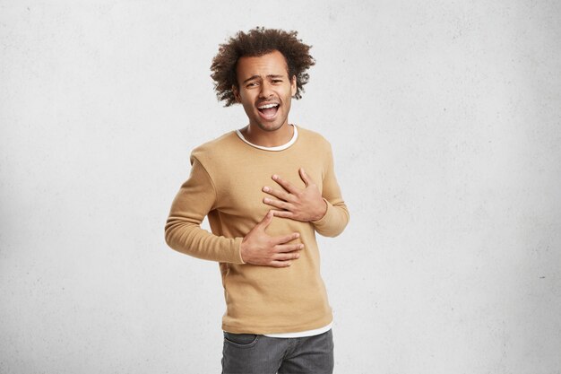 Portrait of young Afro American man can`t stop laughing, keeps hands on stomach