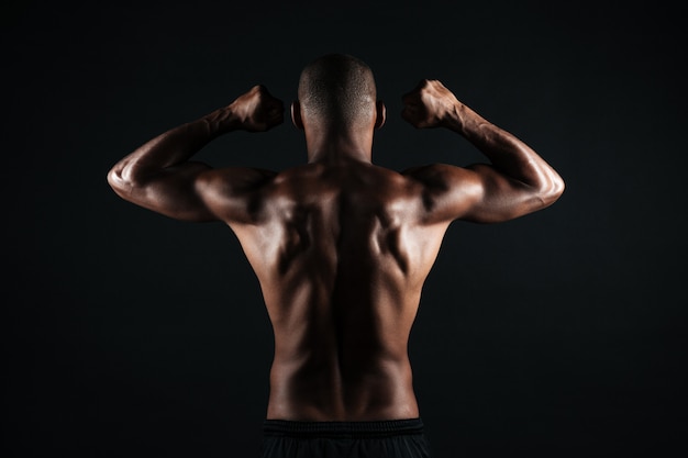 Portrait of young afro american sports man, standing back, showing musculs