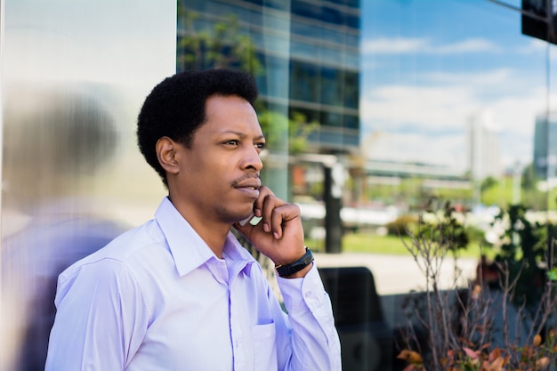 通りで屋外で携帯電話で話している若いアフロのビジネスマンの肖像画。ビジネスコンセプトです。