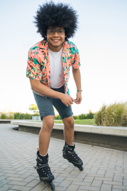 Portrait of young afro latin man looking at camera while rollerskating outdoors on the street. Sports concept. Urban concept.