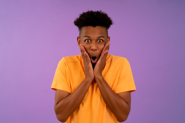 Portrait of a young afro man with shocked expression while standing against isolated background.