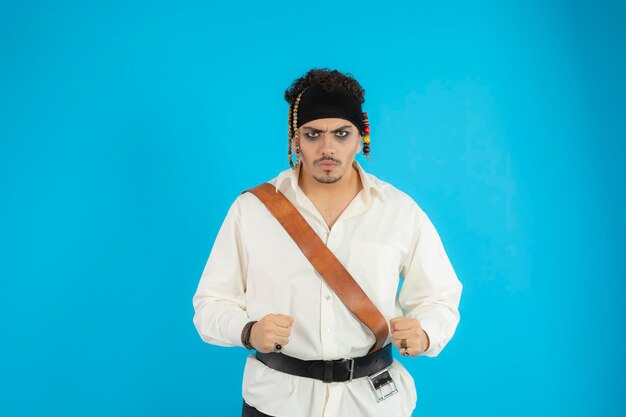 Портрет молодого сердитого пирата стоит на синем фоне. Фото высокого качества