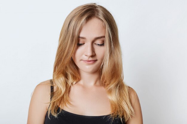 Portrait of young appealing blonde female looks pensively down