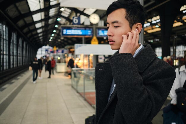 지하철 역에서 신중하게 기차를 기다리는 무선 이어폰을 끼고 있는 젊은 아시아 사업가 초상화