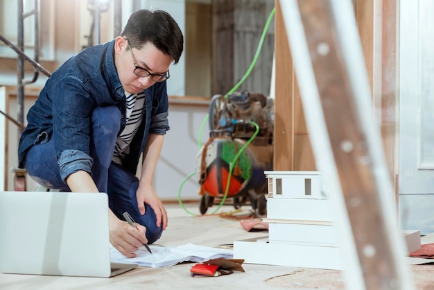 Free photo portrait of young asian contractor carpenter site checking blueprint on floor with concentrate and focus at home renovate site construction background