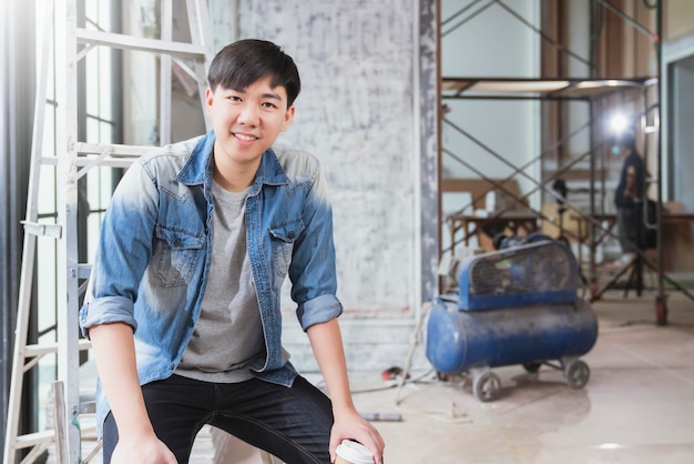若いアジアの請負業者の大工の肖像画は、自宅で自信を持って笑顔でサイト建設の背景を改修します