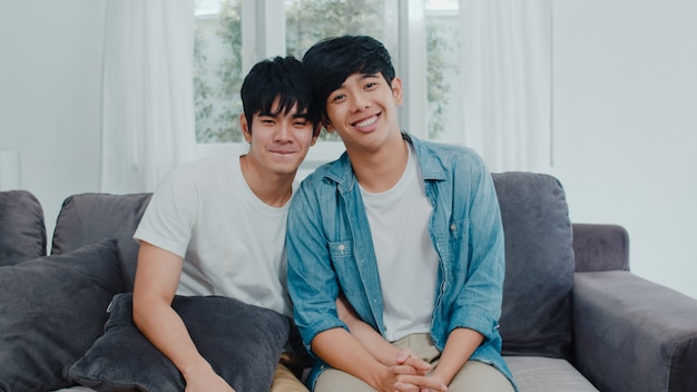 Free photo portrait young asian gay couple feeling happy smiling at home. asian lgbtq+ men relax toothy smile looking to camera while lying on sofa in living room at home in the morning .