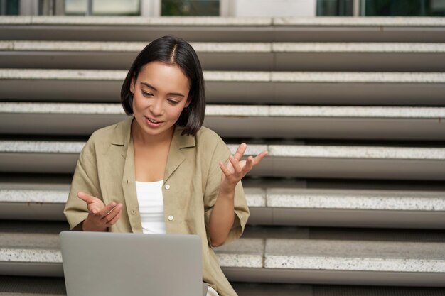 Portrait of young asian girl student talks at laptop video chat speaking during online meeting sitti