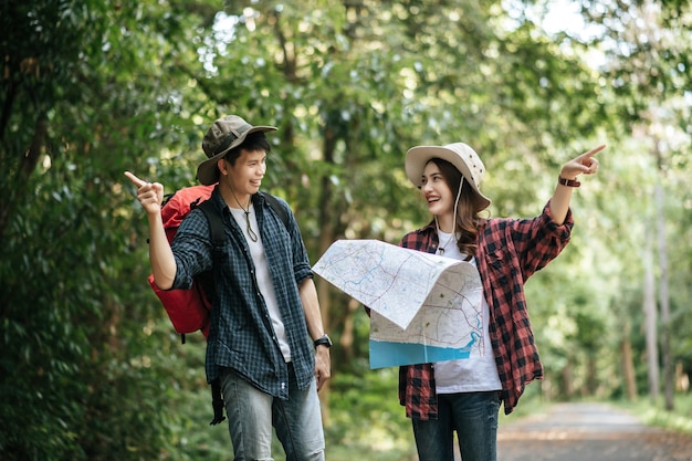 Free Photo portrait young asian handsome man with backpack and trekking hat and pretty girlfriend standing and checking direction on paper map while walking on forest trail, backpack travel concept