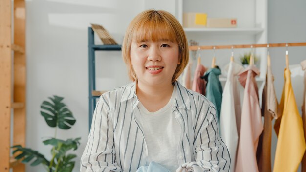 행복 한 미소로 젊은 아시아 여자 패션 디자이너의 초상화, 팔을 넘어 집에서 옷가게를 작업하는 동안 정면을보고