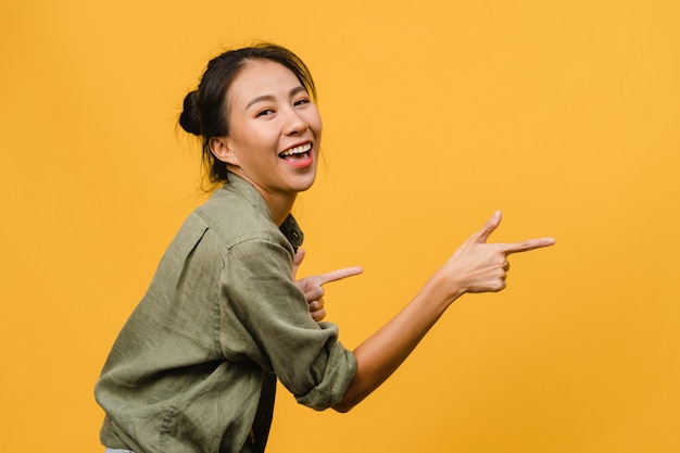 陽気な表情で笑っている若いアジアの女性の肖像画は、黄色の壁に隔離されたカジュアルな布の空白のスペースで素晴らしい何かを示しています。表情のコンセプト。