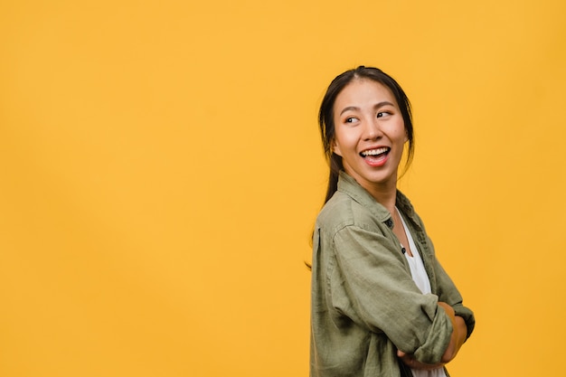 Free photo portrait of young asian lady with positive expression, arm crossed, smile broadly, dressed in casual cloth over yellow wall. happy adorable glad woman rejoices success. facial expression concept.