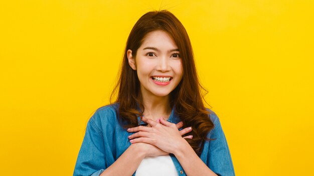 Portrait of young Asian lady with positive expression, joyful and exciting, dressed in casual clothing and looking at the camera over yellow wall. Happy adorable glad woman rejoices success.