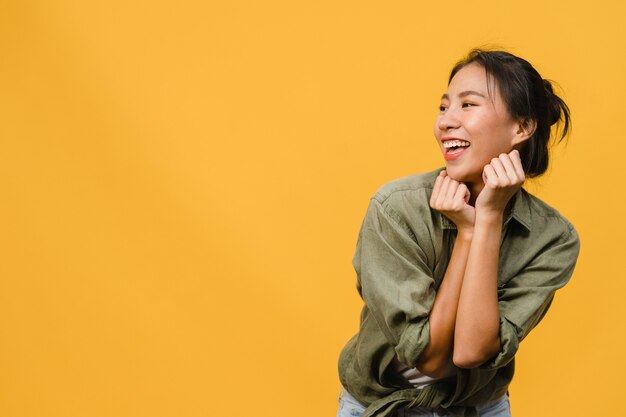 긍정적인 표정을 한 젊은 아시아 여성의 초상화는 노란 벽 위에 평상복을 입고 활짝 웃고 있습니다. 행복하고 사랑스러운 기쁜 여자는 성공을 기뻐합니다. 표정 개념입니다.