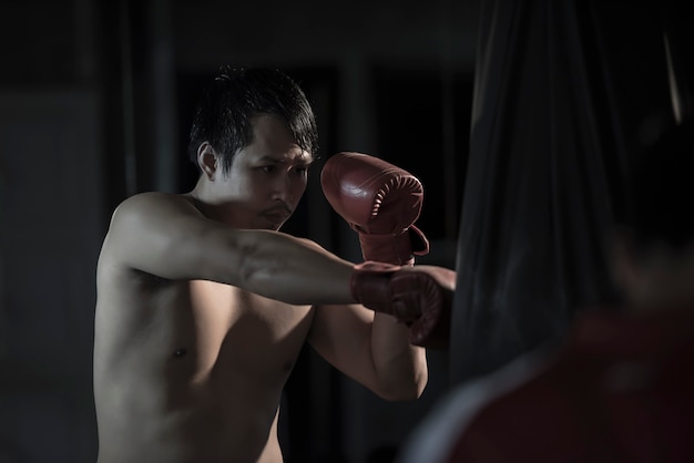 Portrait of a young asian man practicing boxing on a punching bag at gym.