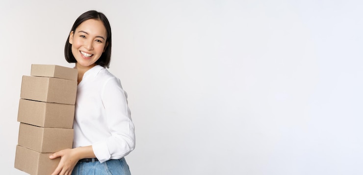 無料Photo ボックスを保持している若いアジアの女性の肖像画は、配達商品を運ぶ韓国の女性起業家は、白い背景の立っている注文を組み立てます