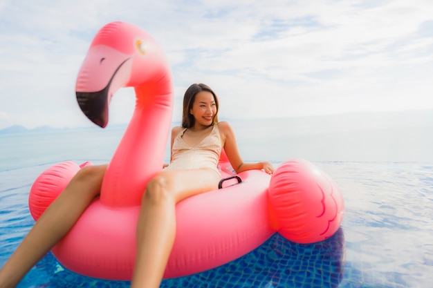 Portrait young asian woman on inflatable float flamingo around outdoor swimming pool in hotel resort
