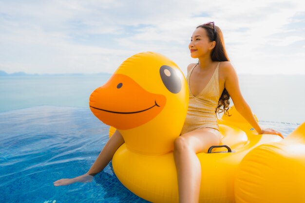 Женщина портрета молодая азиатская на раздувной утке желтого цвета поплавка вокруг открытого бассейна в гостинице и курорте