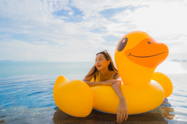 Portrait young asian woman on inflatable float yellow duck around outdoor swimming pool in hotel and resort