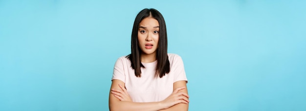 Free photo portrait of young asian woman listening with confused shocked face expression standing in tshirt ove