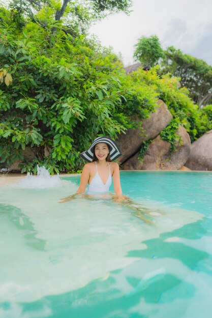 Женщина портрета молодая азиатская ослабляет улыбку счастливую вокруг открытого бассейна в курорте гостиницы с видом на океан моря