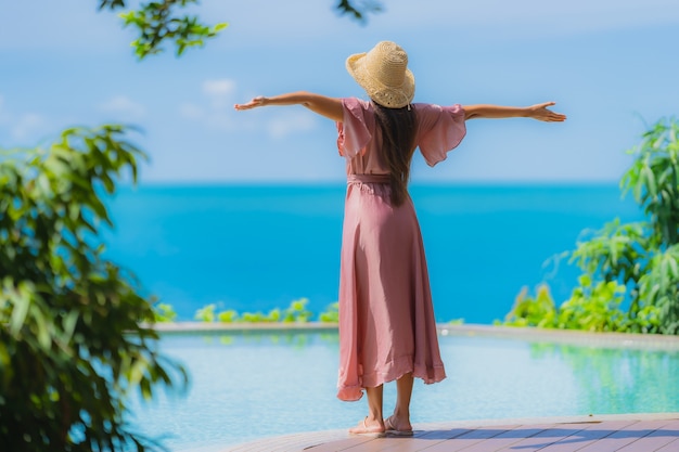 Portrait young asian woman relax smile happy around outdoor swimming pool in hotel resort with sea ocean view