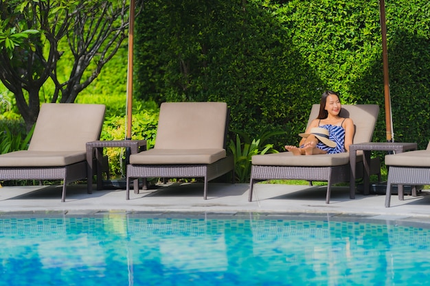 Женщина портрета молодая азиатская ослабляет улыбку счастливую вокруг открытого бассейна в курорте гостиницы с видом на океан моря
