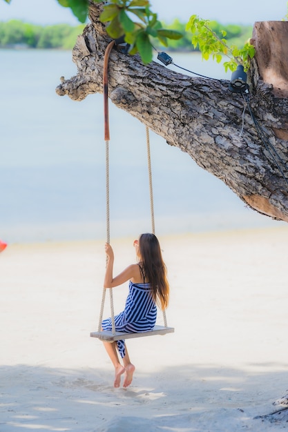 Портрет молодой азиатской женщины, сидя на качели веревку и море вокруг пляжа море океан кокосовой пальмы