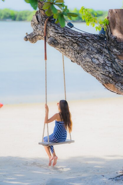 해변 바다 바다 코코넛 야자 나무 주위에 스윙 로프와 바다에 앉아 세로 젊은 아시아 여자