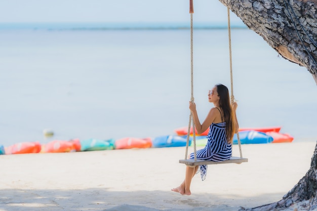 Portrait young asian woman sitting on swing rope and sea around beach sea ocean coconut palm tree 