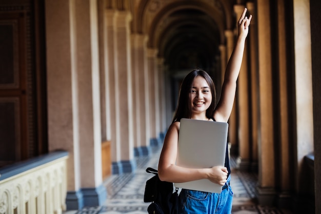 大学やカレッジでスマートで幸せなポーズでラップトップまたはタブレットを使用して若いアジア女性学生の肖像画