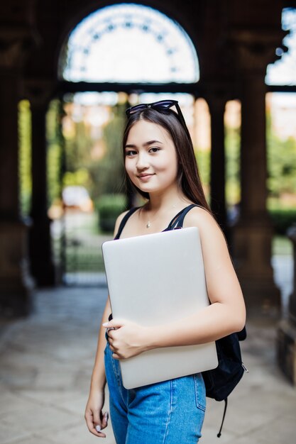 Портрет молодого азиатского студента женщины используя компьтер-книжку или таблетку в умном и счастливом представлении в университет или колледж