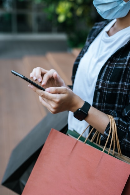 Foto gratuita ritratto di giovane donna asiatica che indossa una maschera di protezione seduta sulle scale con un sacchetto di carta per la spesa shopping