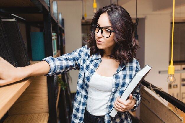 本を探している図書館で黒いガラスの肖像若い魅力的なブルネットの女性。賢い学生、勉強の時間、いい仕事、学術。