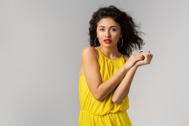 Portrait of young attractive exotic woman in yellow stylish dress, red lips, natural look, pure skin, smiling, isolated, summer season style, fashion trend, wind blowing in curly hair