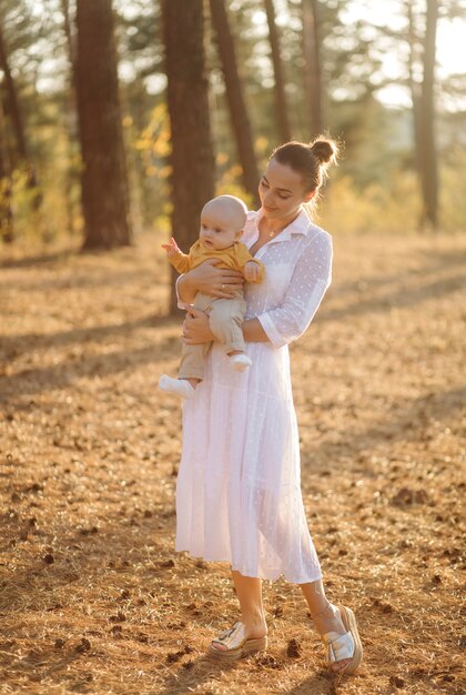 Portrait of young attractive family with little baby son, posing in beautiful autumn pine forest at sunny day. Handsome man and  his pretty brunette wife