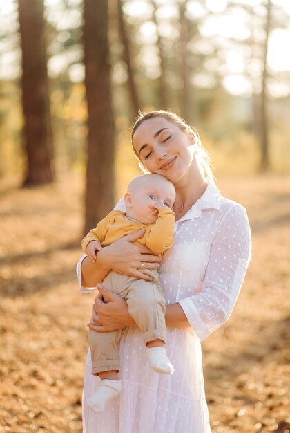 Portrait of young attractive family with little baby son, posing in beautiful autumn pine forest at sunny day. Handsome man and  his pretty brunette wife