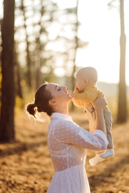 Portrait of young attractive family with little baby son, posing in beautiful autumn pine forest at sunny day. Handsome man and  his pretty brunette wife