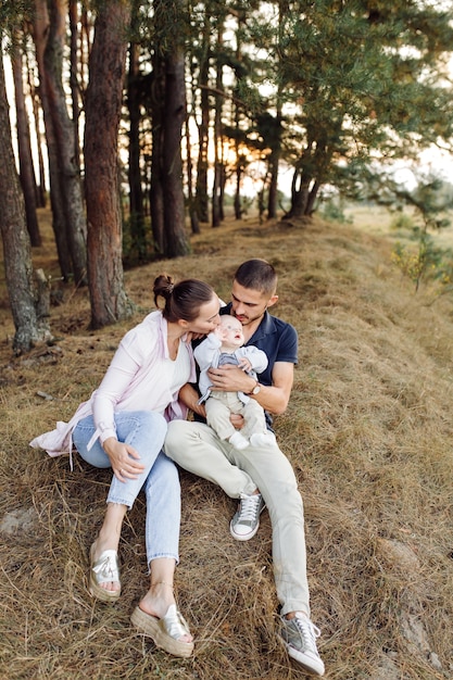 晴れた日に美しい秋の松林でポーズをとって、小さな赤ちゃんの息子と若い魅力的な家族の肖像画。ハンサムな男と彼のかなりブルネットの妻