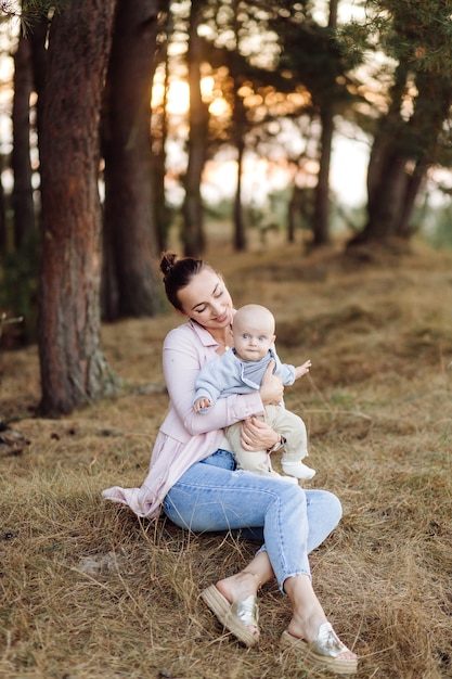 Portrait of young attractive family with little baby son, posing in beautiful autumn pine forest at sunny day. Handsome man and  his pretty brunette wife