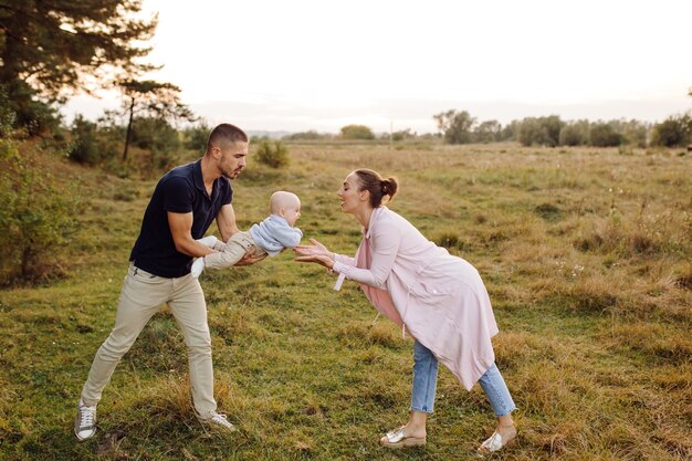 Portrait of young attractive family with little baby son, posing in beautiful autumn pine forest at sunny day. Handsome man and  his pretty brunette wife