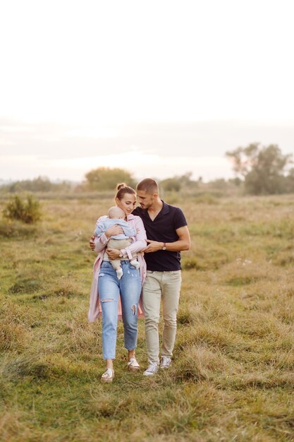 Portrait of young attractive family with little baby son, posing in beautiful autumn pine forest at sunny day. Handsome man and  his pretty brunette wife