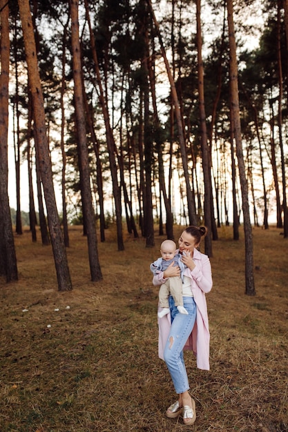 Portrait of young attractive family with little baby son, posing in beautiful autumn pine forest at sunny day. Handsome man and  his pretty brunette wife